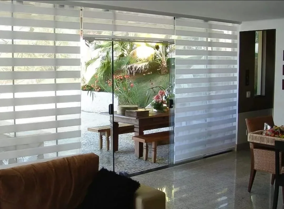 Cortina rolô double vision em porta de vidro de sala com vista para o jardim