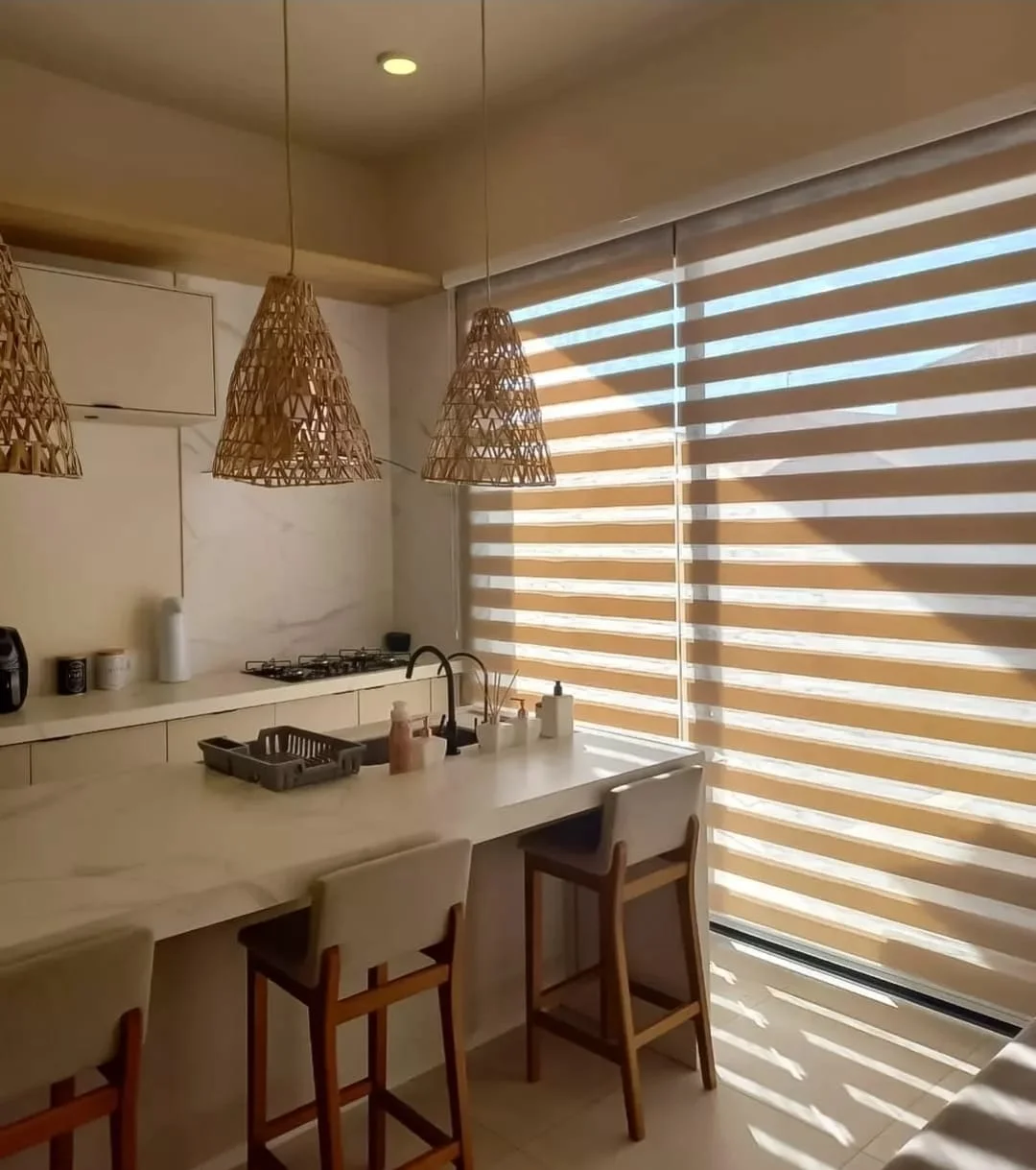 Cortina rolô double vision bege em cozinha gourmet com ilha e luminárias