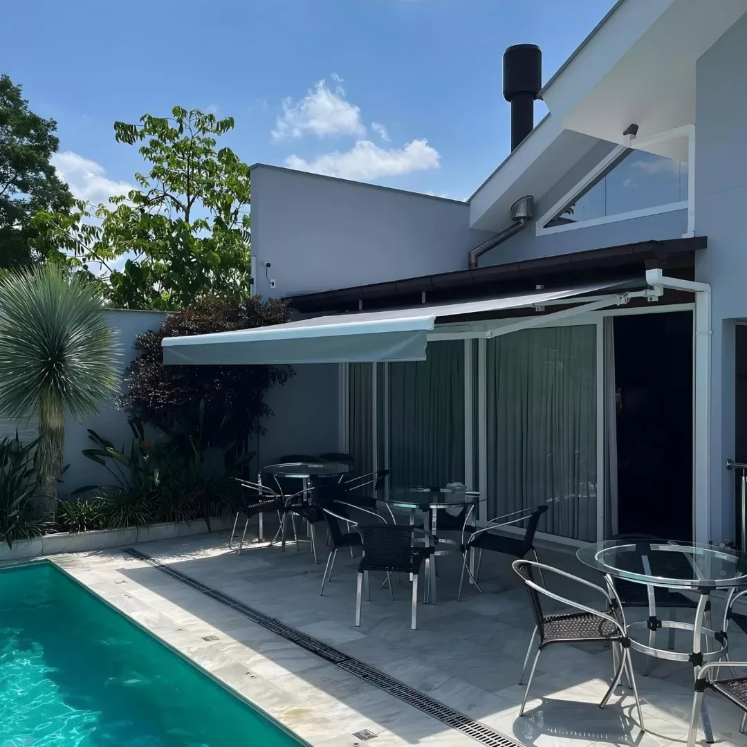 Toldo retrátil branco sobre varanda com mesas ao lado da piscina